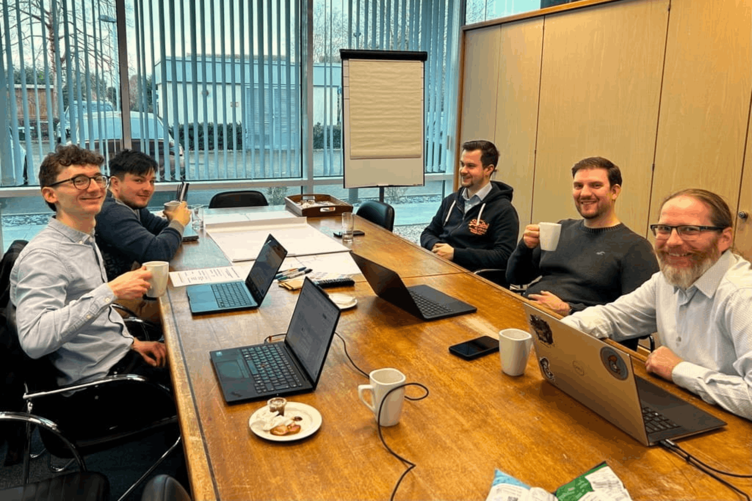 IT support Essex TechWyse team, with five members of the management team sitting around a table with laptops, smiling at the camera.